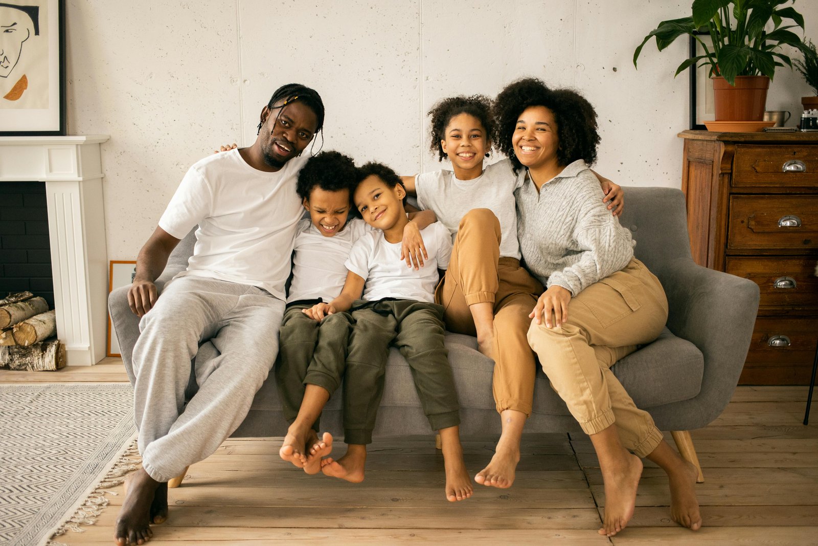 pexels photo 7114420 7114420 Full body of cheerful African American parents with children looking at camera while sitting on sofa in room with fireplace